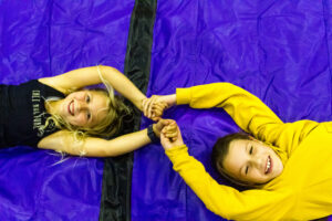 two smiling children smiling, theyre lying on their backs on a blue mat their hands clasped above their headss